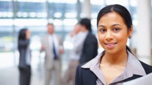 Administrative assistant stands in a large open office building lobby holding papers and smiling to girls