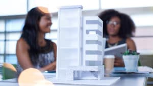 Woman architecture student with an architect designing a model of an 8 story building with balconies