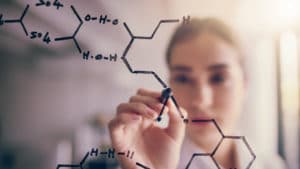 Female chemical engineer uses a black marker to draw a chemistry symbol diagram on a clear glass board