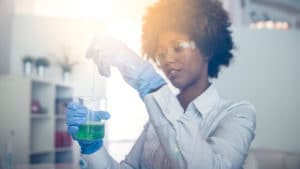 Female chemist in a white lab coat and blue nitrile gloves performs chemistry experiment mixing liquids in a beaker