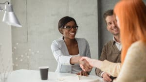 Woman human resource manager shakes hands with new diverse group of employees around a white table with a cup of coffee