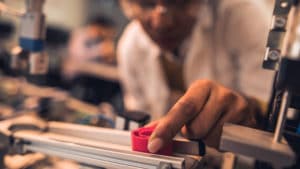 Woman materials engineer at a laboratory workbench examining red piece of material with industrial tools