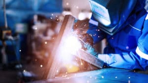 Woman mechanical engineer welding iron beams to build a structure support as bright sparks fly from the metal