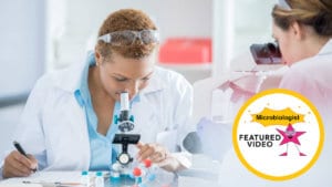 Woman microbiologist in white lab coat and safety glasses on her head examines molecules with a microscope in laboratory