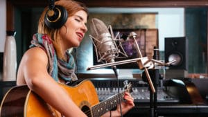 Professional career musician young woman playing acoustic guitar and singing into a microphone in a recording studio