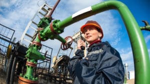 Woman petroleum engineer in a dark protective coat talking on a portable radio and working on oil rig platform at sea