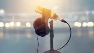 Announcer golden microphone on a black mic stand with headphones on stage with white footlights in background