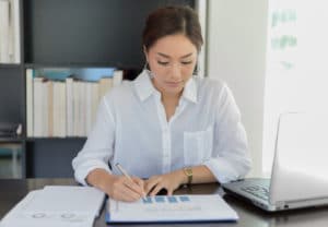 Woman at office desk making notes on printed financial bar charts