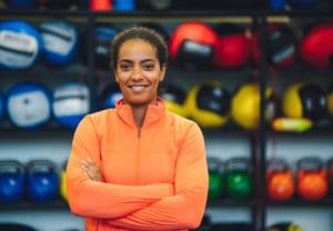 Woman coach in orange jacket in front of exercise room