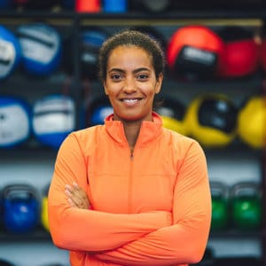 Woman coach in orange jacket in front of exercise room