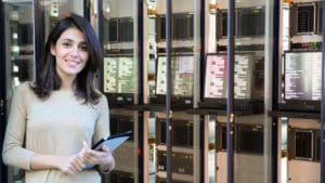 Woman computer systems analyst with a notebook in hand stands in front of a large stacked array of computer screens