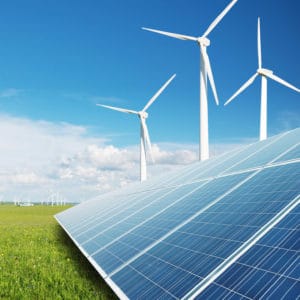 Energy Career Cluster image of clean solar panels on bright green grass in front of white wind turbines against a blue sky