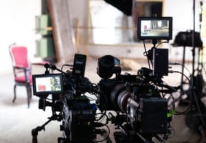 Video cameras and monitors on tripods focused on living room film set