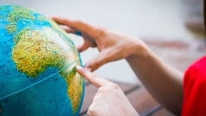 Woman geographer studies a world globe on a brown table with a finger pointed to a country in the African continent