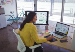 Woman sitting at desk with two computer monitors inside of a contemporary office setting