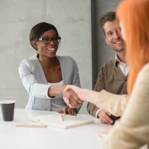 Woman human resource manager shakes hands with new diverse group of employees around a white table with a cup of coffee