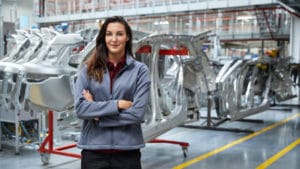 Woman industrial production manager stands in a factory warehouse assembly with a gray shiny floor and red racks of automobile parts