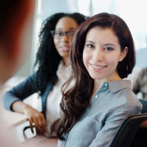 Woman labor relations specialist smiles at camera and sits around a table with a diverse group of employees in a work setting