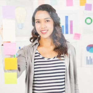 Woman market researcher in black and white horizontally striped shirt stands in front of colorful charts and sticky notes