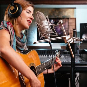 Musician Career - young woman playing acoustic guitar and singing into a microphone in a recording studio