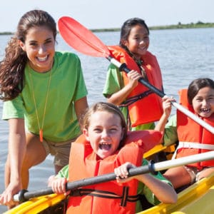 Young woman recreation worker leads a group of girls wearing orange life vests on a boat expedition on a freshwater lake