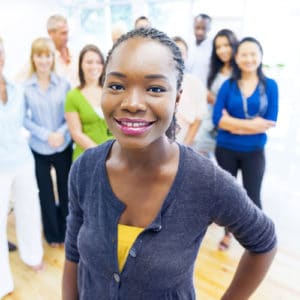 Woman sociologist in navy purple shirt stands and smiles in front of a diverse group of fellow team members