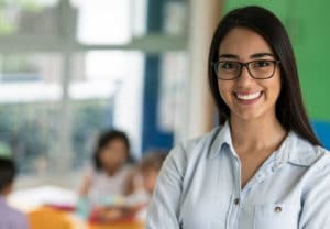 Education College Major - Woman with glasses smiling in front of a classroom with students