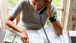 Female book and literary editor speaks on the phone while looking over a written manuscript laid out on table