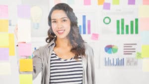 Woman market researcher in black and white horizontally striped shirt stands in front of colorful charts and sticky notes