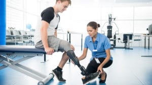 Woman orthotist prosthetist in light blue doctors shirt works with a patient in an exercise room to adjust his artificial leg