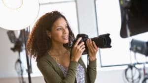 Woman photographer using a camera with a long lens taking photographs in photography studio with large reflectors and soft lights