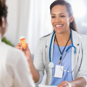 Woman psychiatrist in light blue medical scrubs and white coat smiles at a patient and shows a recommended prescription