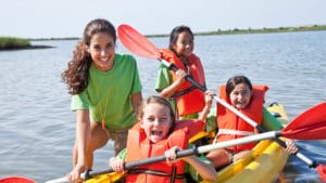 Young woman recreation worker leads a group of girls wearing orange life vests on a boat expedition on a freshwater lake