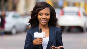 Woman reporter holds a TV news microphone reporting for a television station standing in front of a street scene