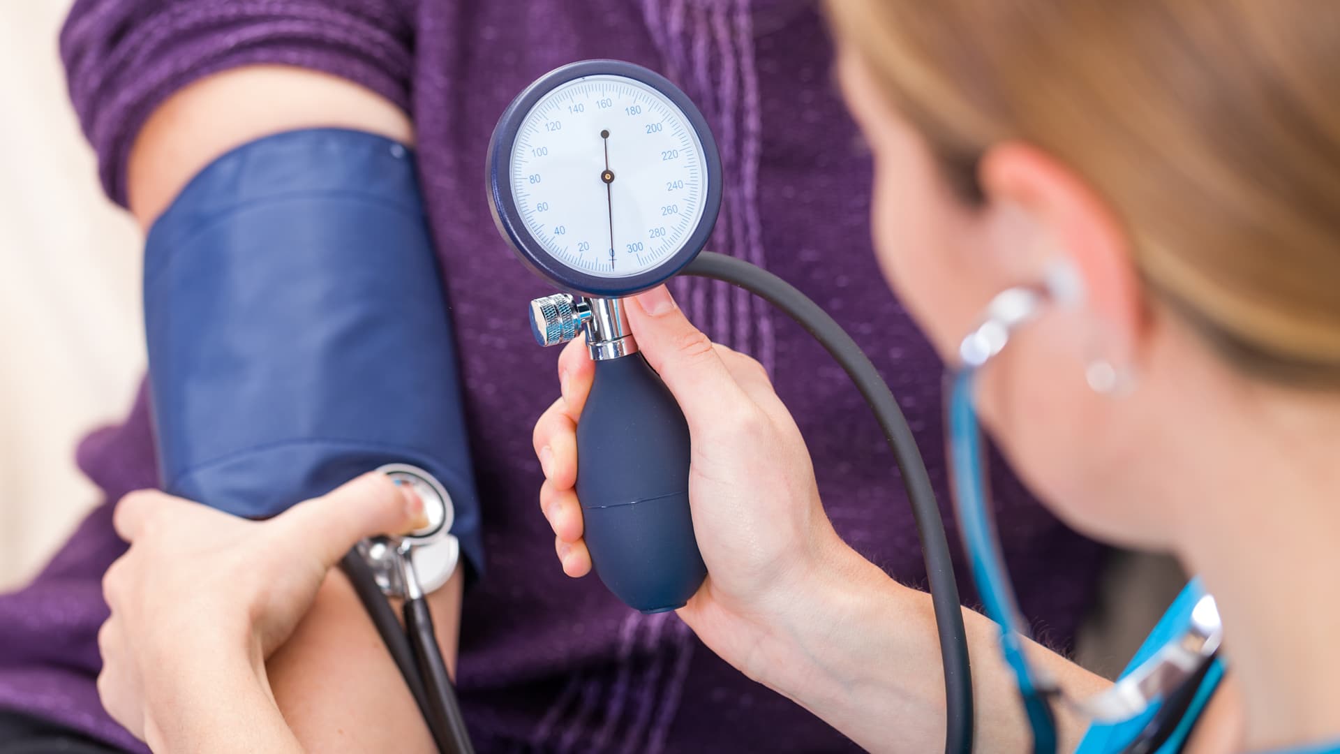 Woman physicians assistant (PA) measures the blood pressure of a patient at a doctor's office wearing a purple sweater