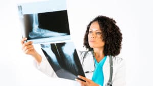 Woman podiatrist in bright blue shirt and white lab coat examines and compares two x-ray images of an injured foot