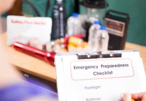 Emergency Management College Major - Woman with emergency supply kit making notes on an emergency preparedness checklist