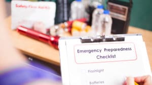 Woman emergency management director writes on emergency preparedness checklist notepad next to table with flashlight and other gear