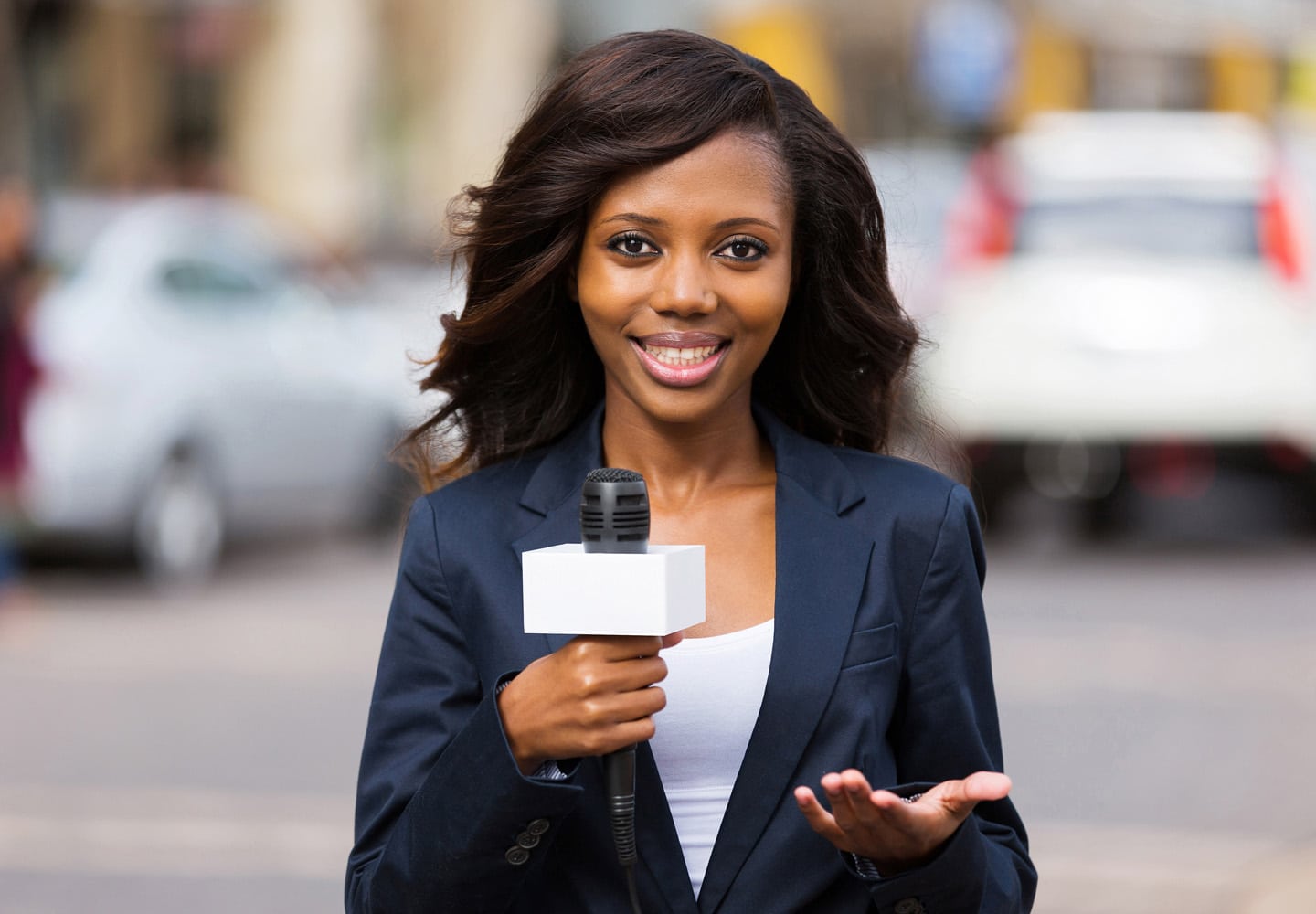 Woman speaking while standing in front of a city street holding a reporter's microphone
