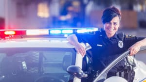 Woman police officer and detective smiles standing in her uniform next to her patrol car at night on a city street