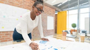 Female advertising and promotions manager leans over a table in a bright office to study advertisement options