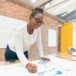 Female advertising and promotions manager leans over a table in a bright office to study advertisement options