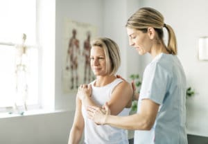 Occupational therapist works with a client bending her elbow in room with anatomy poster