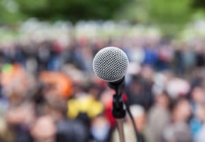 Social Impact image of empty microphone on stage in front of large outdoor peaceful crowd