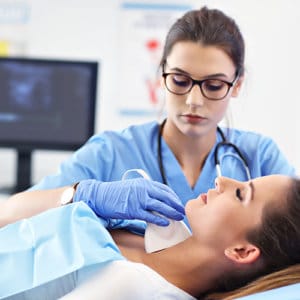 Sonography Career - Female sonographer in blue uniform performs ultrasound on woman's neck