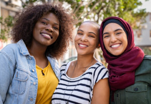 Three women of different ethnicities smiling together in a park