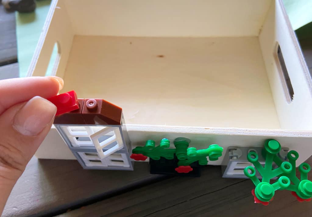 Hand adds red lego decoration to fron top of model house