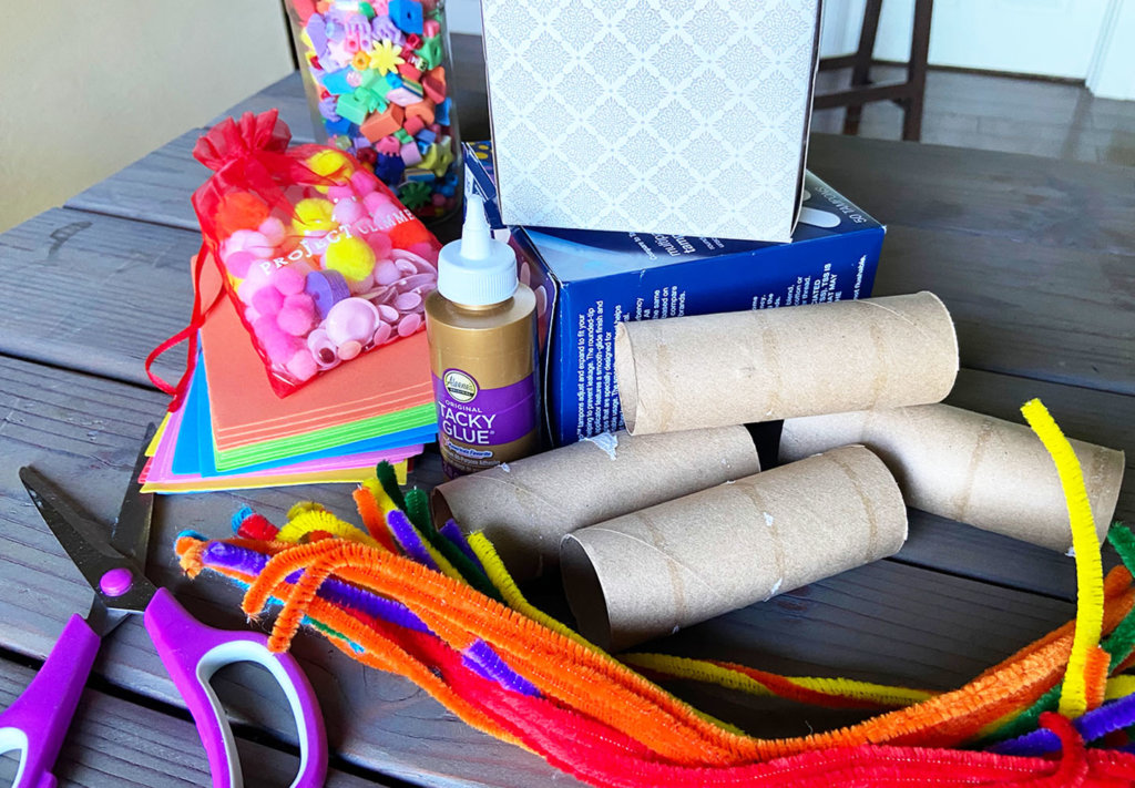 Colorful assortment of cardboard tubes, tissue box, pipe cleaners, decorative yarn, glue and scissors to make an obstacle course group activity project