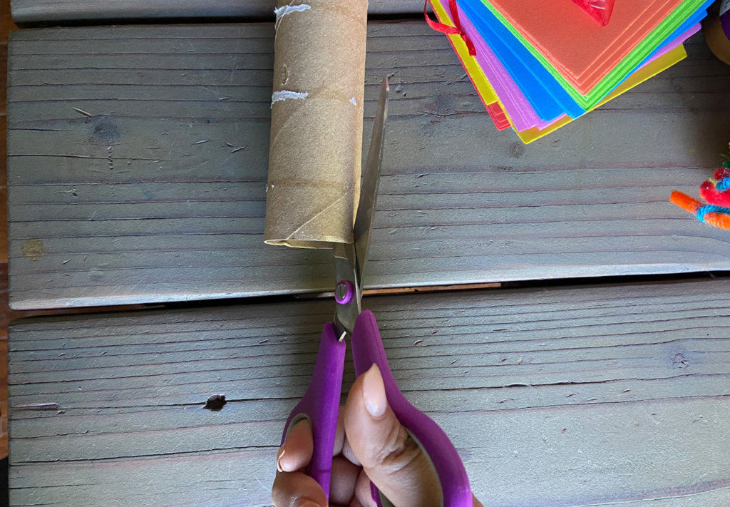 Cutting the cardboard tube with scissors to create a track for the ping pong ball obstacle course