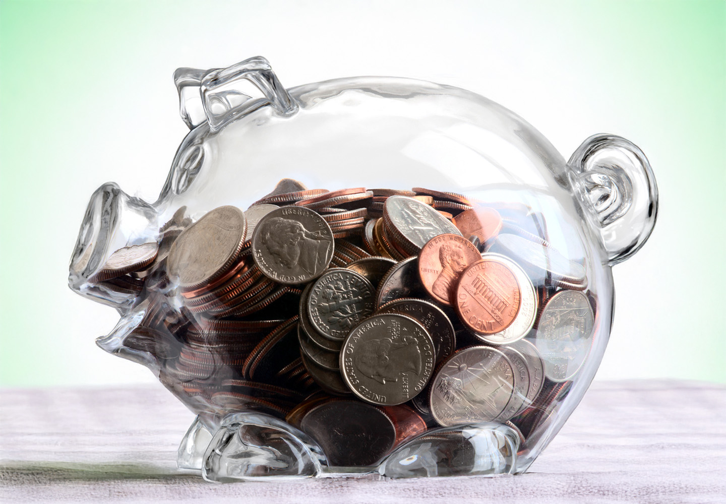 Transparent Piggy Bank Partially Filled With Coins With Green Background